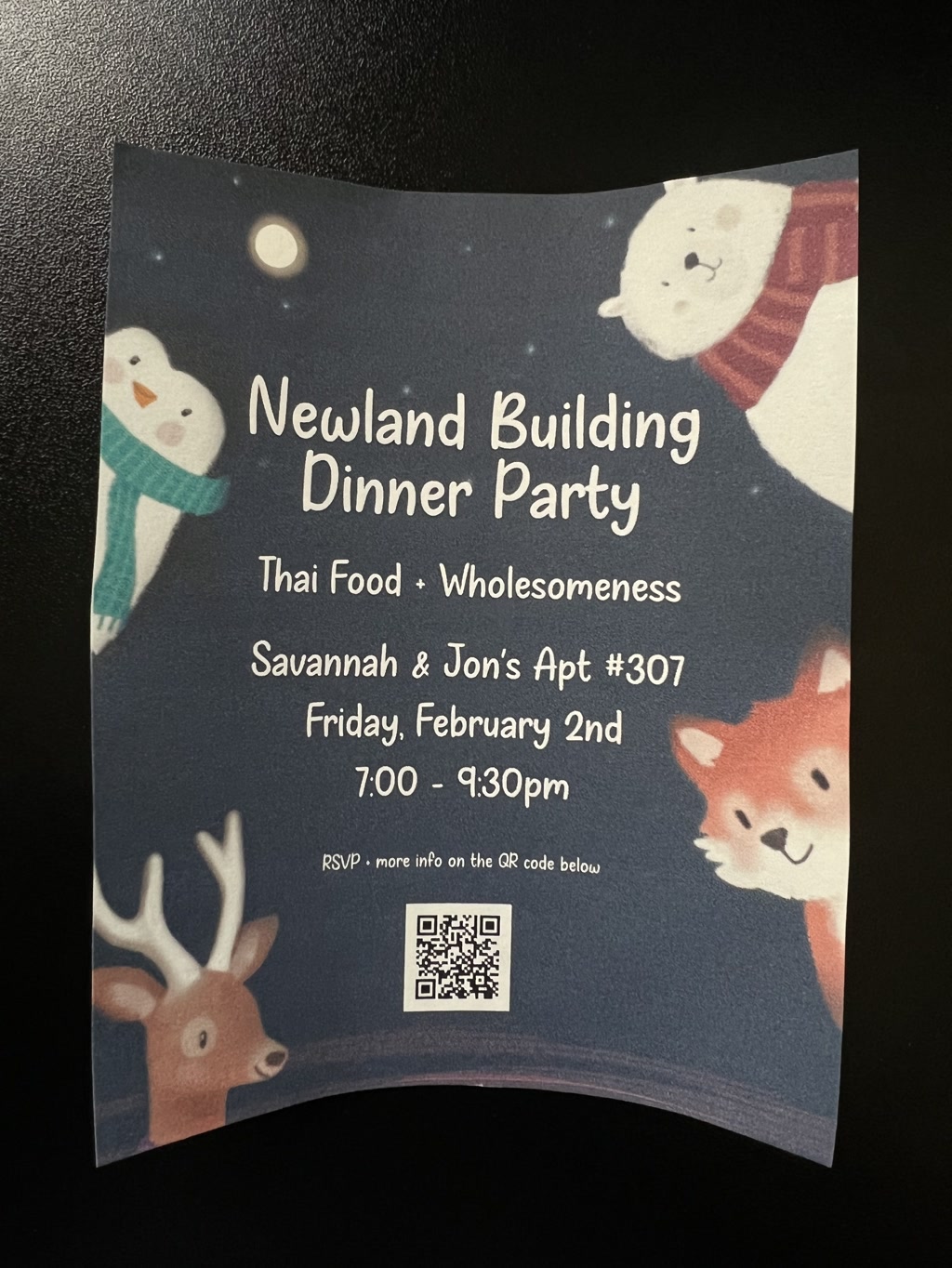 A curved paper invitation with a night sky background and a cute animal motif features a snowman, bear, deer, and fox in cartoon style. The invitation is for the Newland Building Dinner Party, emphasizing Thai Food and Wholesomeness, hosted by Savannah & Jon at Apartment #307 on Friday, February 2nd from 7:00 to 9:30 pm. Attendees are directed to RSVP and find more information via a QR code at the bottom of the invitation.